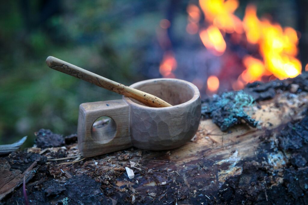 Finnish wooden Kuksa cup resting on a log in a natural forest setting.